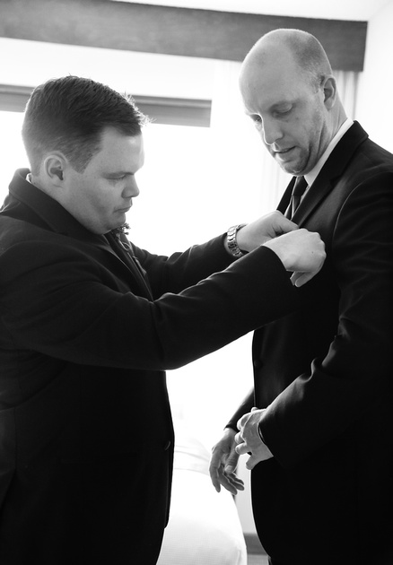 Wedding photography, the best man helps the groom with his pocket square. 