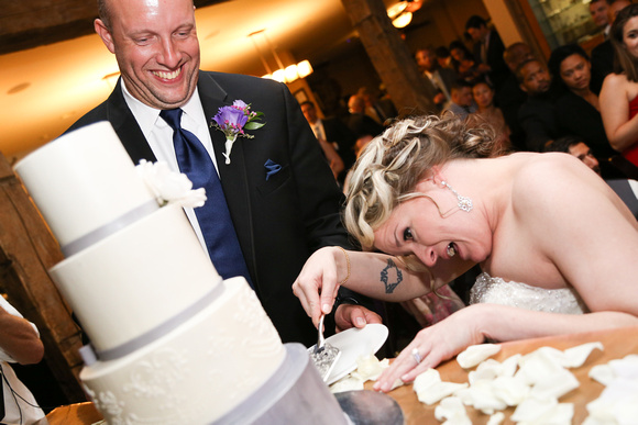Wedding photography, the groom laughs as he watches his silly bride cut the cake. 