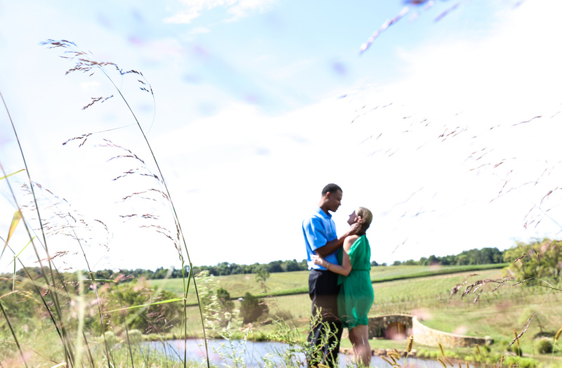 Engagement photography: a couple embraces while standing in an open field at a vineyard. 