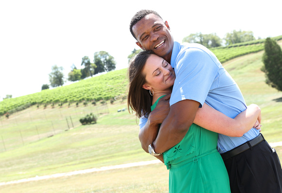 Engagement photography: a man in a blue shirt smiles widely as he hugs his fiancé close. She is wearing a green dress and smiling serenely. 