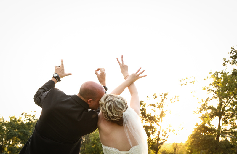 Wedding photography, the bride and groom kiss while holding their hands in the air. They spell the word "love."