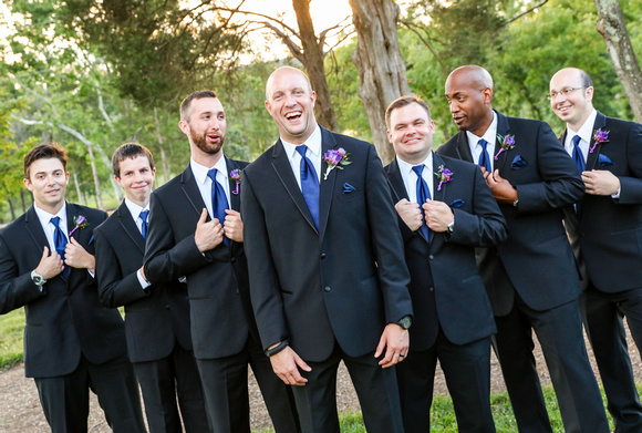 Wedding photography, a groom laughs heartily, flanked by his groomsmen in black suits with blue ties. 