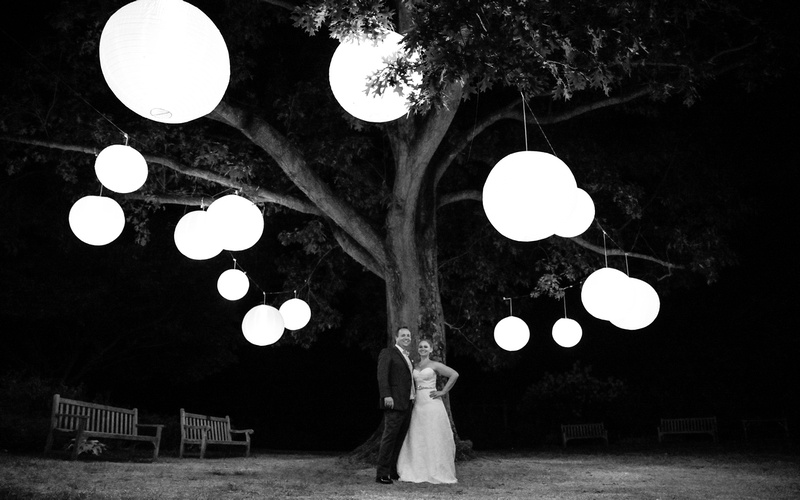 Wedding photography, the bride and groom pose under a large tree with big hanging lanterns. 