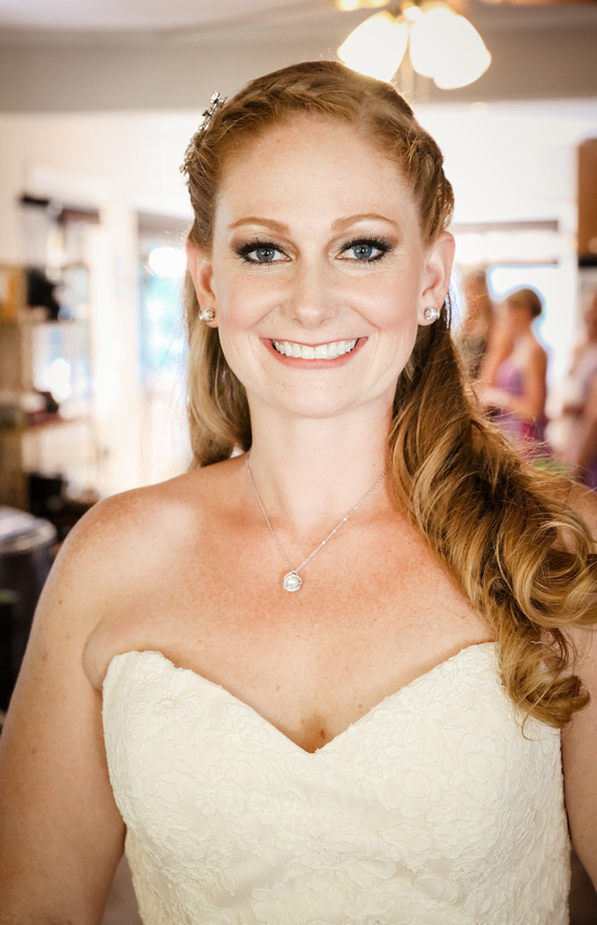 Wedding photography, a smiling bride with long red hair and blue eyes is wearing a sweetheart neckline dress. 