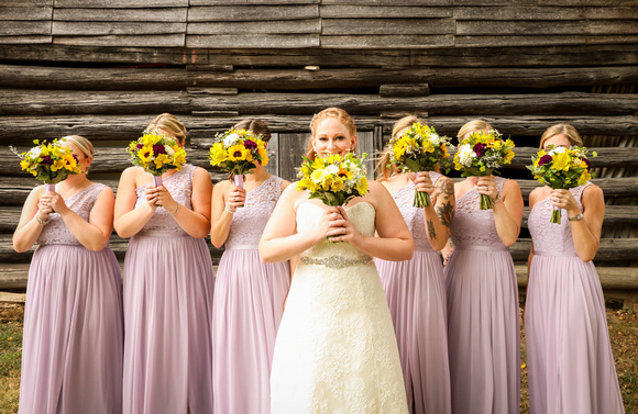 Wedding photography, a bride smiles holding her bouquet. Her bridesmaids hold their bouquets in front of their faces. 