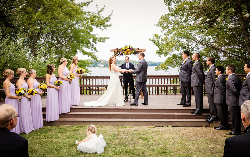 Wedding photography, the ceremony is waterfront with the bride and groom holding hands on the deck. 