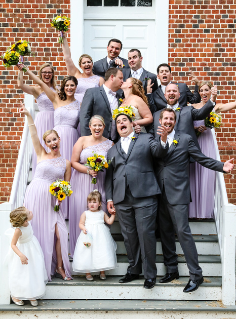 Wedding photography, the wedding party makes silly faces while the bride and groom kiss. 
