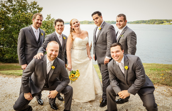Wedding photography, the bride laughs while the groomsmen pose in front of her. They are wearing grey suits with yellow flowers. 