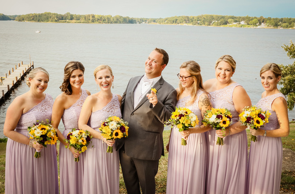 Wedding photography, the groom points to the camera and smiles with the laughing bridesmaids.