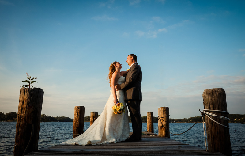 Wedding photography, the bride and groom stand on a pier at sunset gazing at each other. 