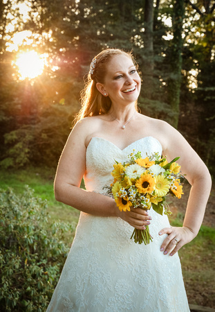 Wedding photography, a bride laughs with the sun shining through the trees behind her. 