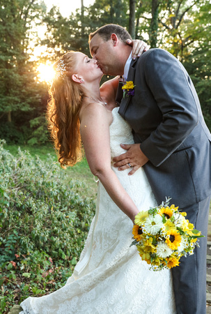 Wedding photography, the groom dips the bride and kisses her. She is holding yellow flowers. 