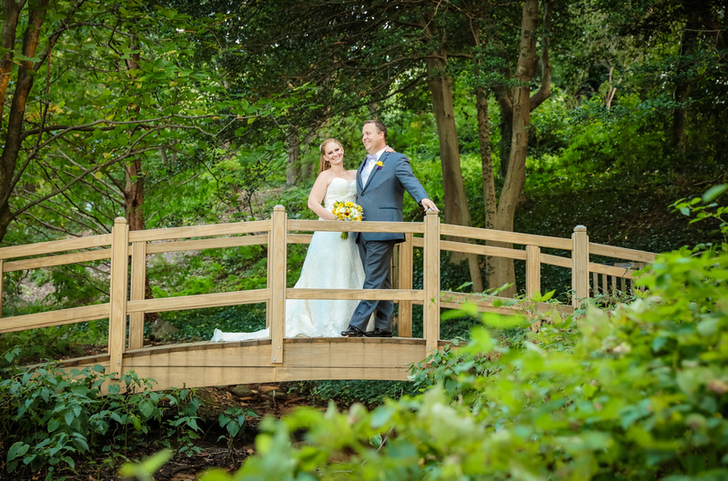 Wedding photography, the bride and groom stand on a bridge in a lush green forest. 