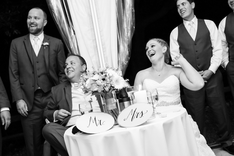Wedding photography, the bride and groom laugh at their sweetheart table during toasts. 