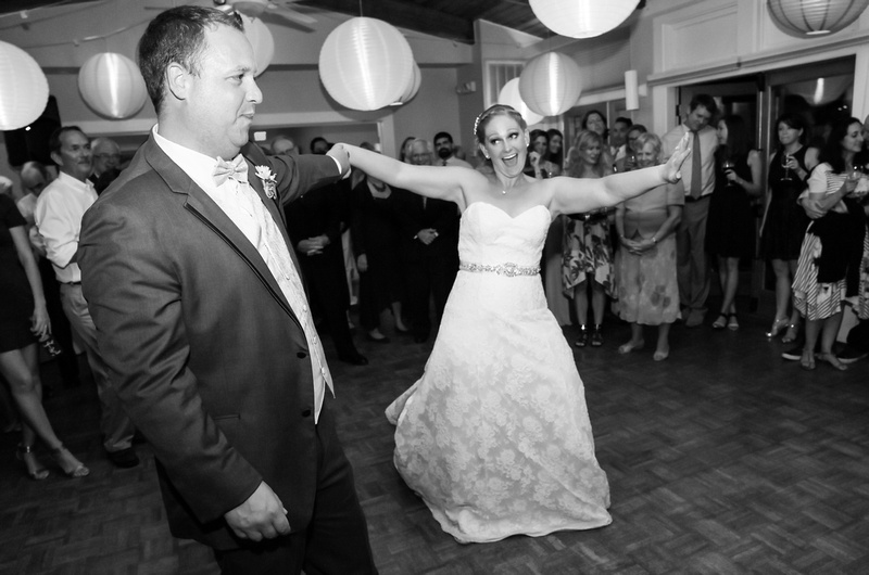 Wedding photography, the bride laughs while dancing with her groom. The ceiling is filled with lanterns. 