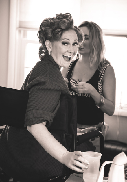 Wedding photography, a bride in a robe with curlers in her hair smiles excitedly at the camera. 