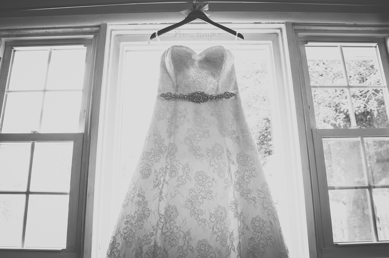 Wedding photography, a white lace gown with beaded embellishments hangs in a picture window. 