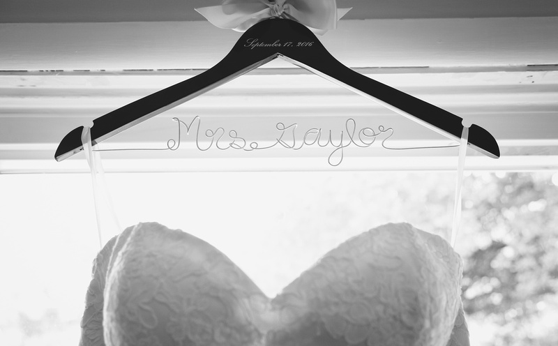 Wedding photography, a white wedding dress hangs on a wooden hanger that reads, Mrs. Gaylor. 