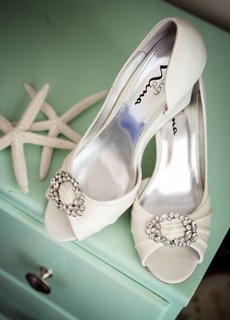 Wedding photography, white satin heels with rhinestones sit next to white starfish on a sea-foam green dresser. 