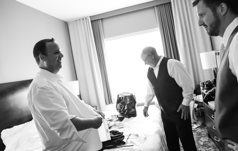 Wedding photography, a groom smiles while getting dressed for his wedding day. 