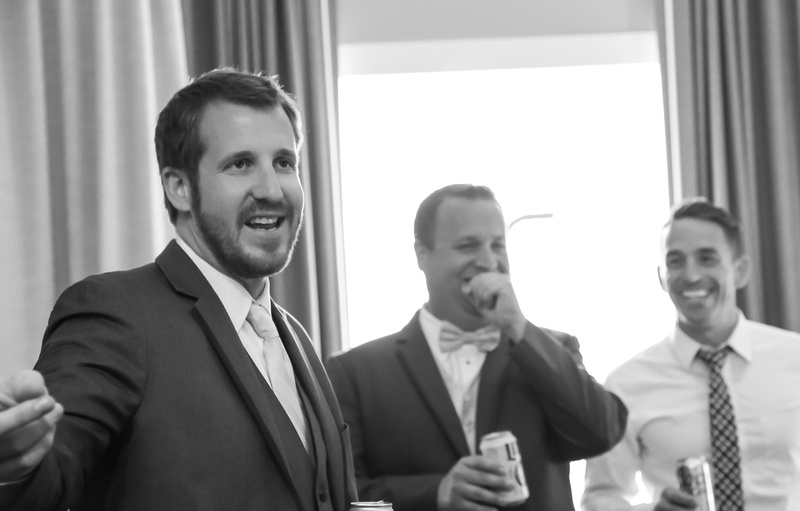 Wedding photography, a groom laughs heartily while his groomsman tells a story. 