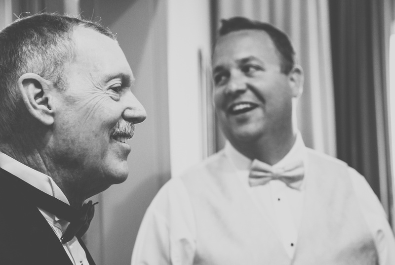Wedding photography, a groom and his father are smiling. They are both wearing bow ties. 