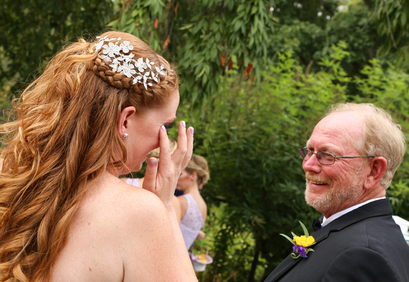 Wedding photography, a red-haired bride wipes away a tear while looking at her father. 