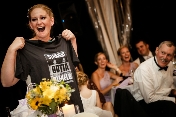 Wedding photography, the bride laughs out loud and holds up a black tee shirt. 