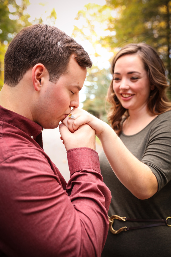 Engagement photography: a young man kisses his fiancé's hand while she smiles. 