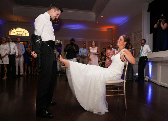 Wedding photography, the groom playfully takes off his jacket while the bride holds out her leg for the garter. 