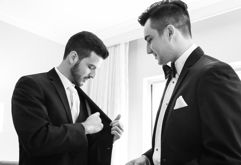 Wedding photography, a groom in a tuxedo smiles as he gives the rings to his best man. 
