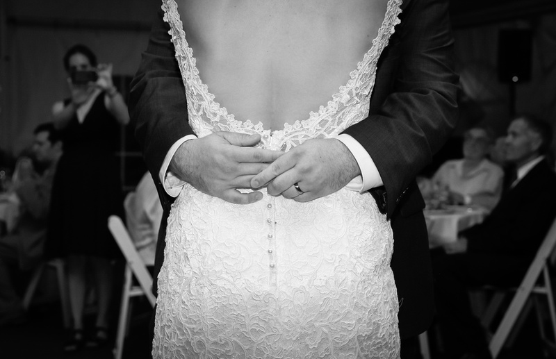 Wedding photography, a closeup shot of a groom's hands wrapped around a bride's back. She wear a low back lace gown. 