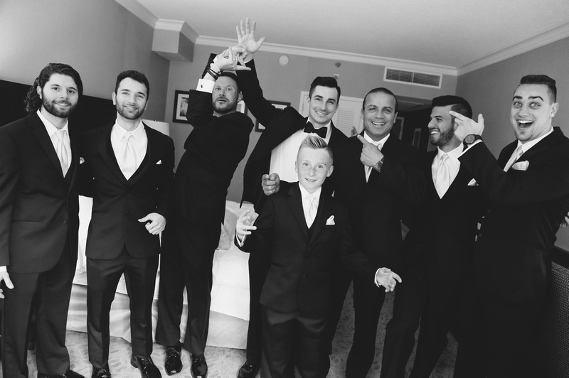 Wedding photography, 7 men and a young boy wearing black tuxedos are laughing. 