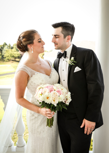 Wedding photography, a bride in an embroidered gown and a groom in a black tuxedo stare into each other's eyes. 
