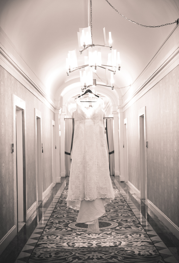 Wedding photography, a wedding gown hangs from a chandelier in a hotel hallway. 