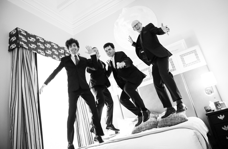 Wedding photography, a groom and his groomsmen jump on the bed in their wedding suits. 