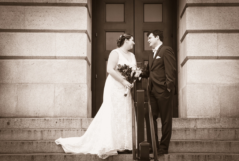 Wedding photography, a bride and groom smile at each other while standing on a city staircase. 