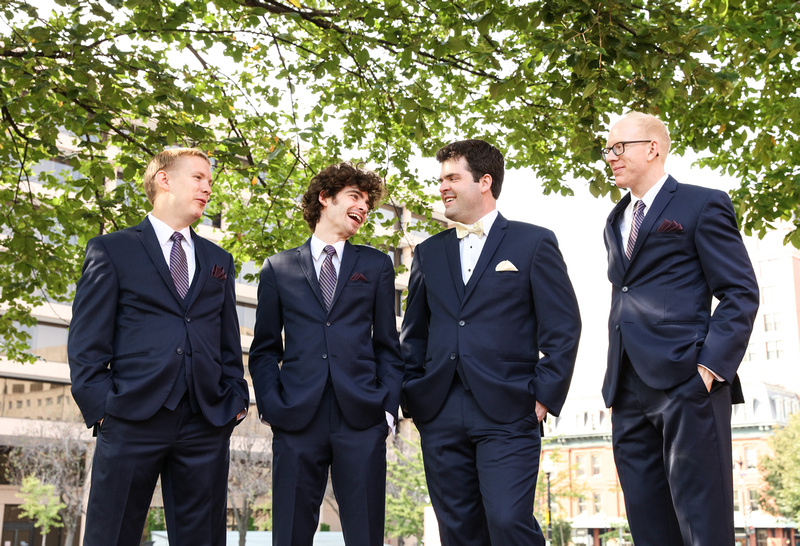 Wedding photography, a groom and groomsmen smile in navy blue suits under a tree limb. 