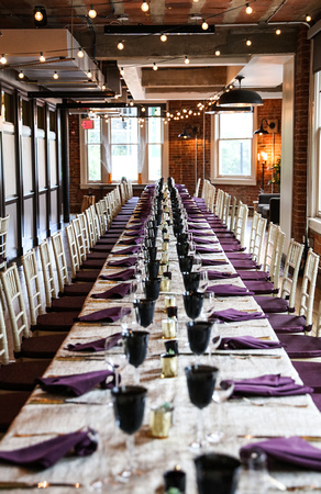 Wedding photography, a long dinner table set with purple napkins and navy blue goblets. 