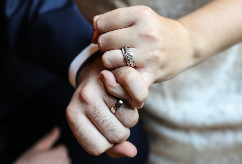 Wedding photography, a closeup of a bride and groom's hands and wedding rings as they link fingers. 