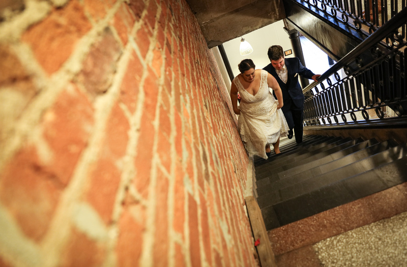 Wedding photography, a bride and groom walk up a stairwell next to a red brick wall. 
