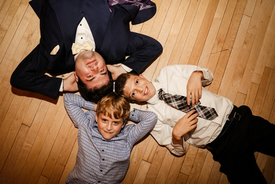 Wedding photography, a groom lays on the hardwood floor with his little cousins. 