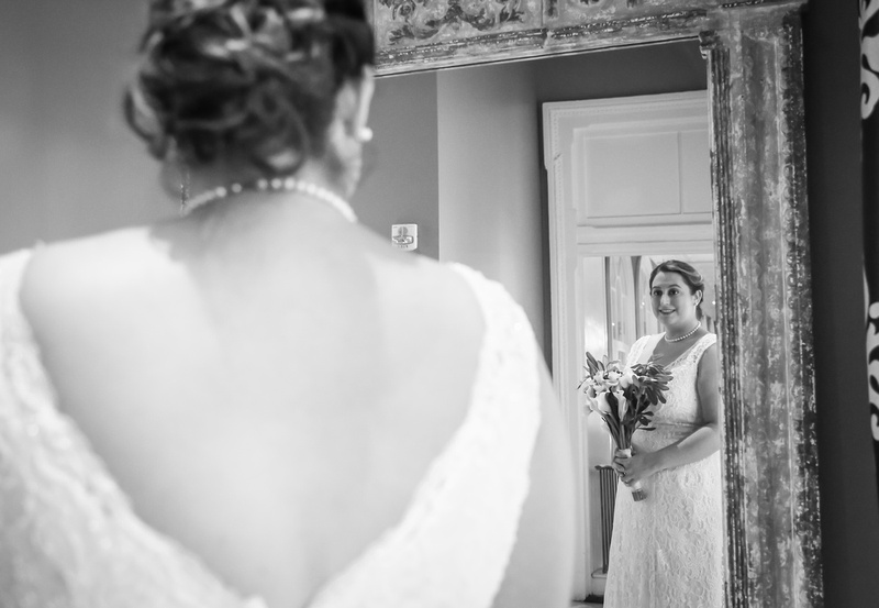 Wedding photography, a bride smiles as she looks at her reflection in the mirror. 