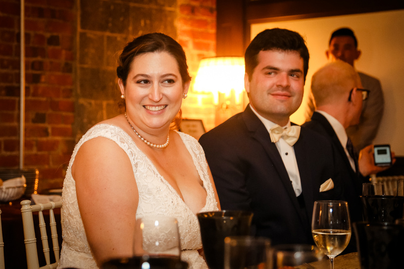 Wedding photography, a bride and groom smile at their dinner table. 