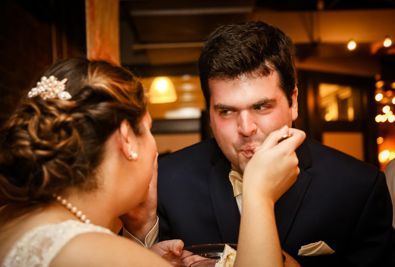 Wedding photography, a bride with pearls in her hair feeds her groom a bite of cake.
