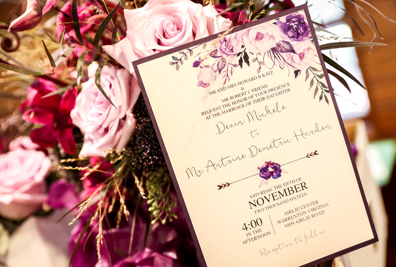 Wedding photography, a purple wedding invitation sits on a bouquet of lavender roses and greenery. 