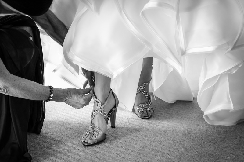 Wedding photography, a black and white image of a bride's feet as her mother puts on her high-heeled diamond shoes. 