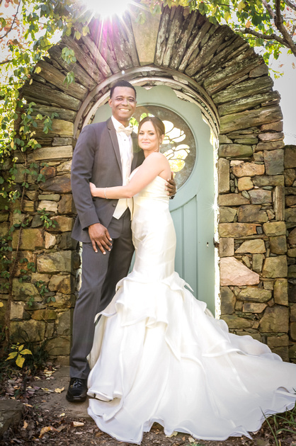Wedding photography, a bride and groom embrace in front of a stone wall with a teal door. The sun is shining. 