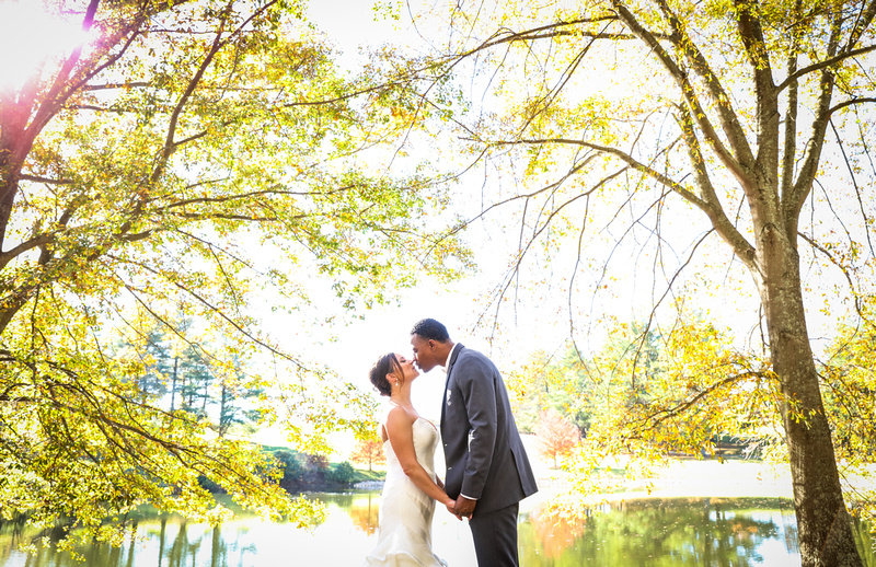 Wedding photography, a bride and groom kiss between two yellow trees and a lake. 
