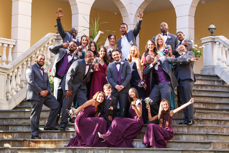 Wedding photography, the bridal party celebrates enthusiastically while standing on a stone staircase. 